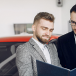 Car salesman showing a brochure to a couple in a dealership, discussing options for purchasing a vehicle